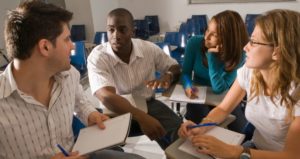 An image of four people in a classroom discussing something.