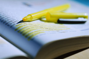 An image of a yellow highlighter pen resting on a book with some text highlighted