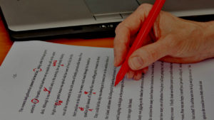 An image showing a hand holding a red pen correcting some work